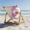 Pink and white trucker hat with 'SALT WATER Vibes' burlap patch resting on a beach chair on sunny white sand with ocean waves in the background.