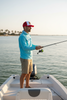 Man wearing red and white Live Salty & Stay Breezy trucker junk hat while fishing on a boat on a sunny Gulf Coast day, casual lifestyle scene.